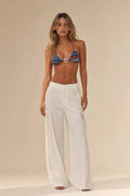 Woman standing in front view wearing white cutout wide leg trousers and patterned bikini top