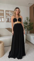 Model wearing black gold-trimmed halter pleated maxi dress from the front