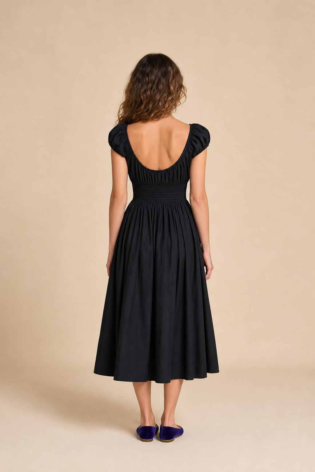 Back view of woman in black smocked midi dress against neutral background