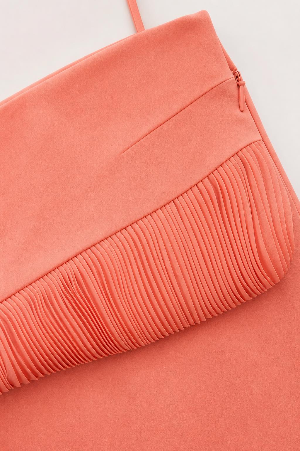Close-up detail of pleated ruffle hem and side zipper on coral skirt