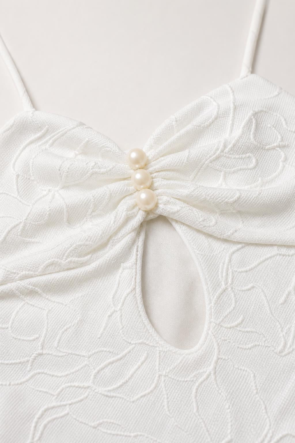 Close-up detail of bodice cutout and faux pearl buttons on white dress