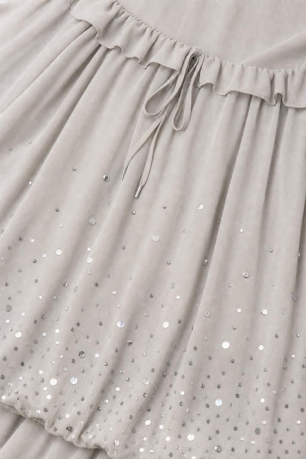 Close-up detail of sequin embellishments and drawstring waist on grey chiffon dress