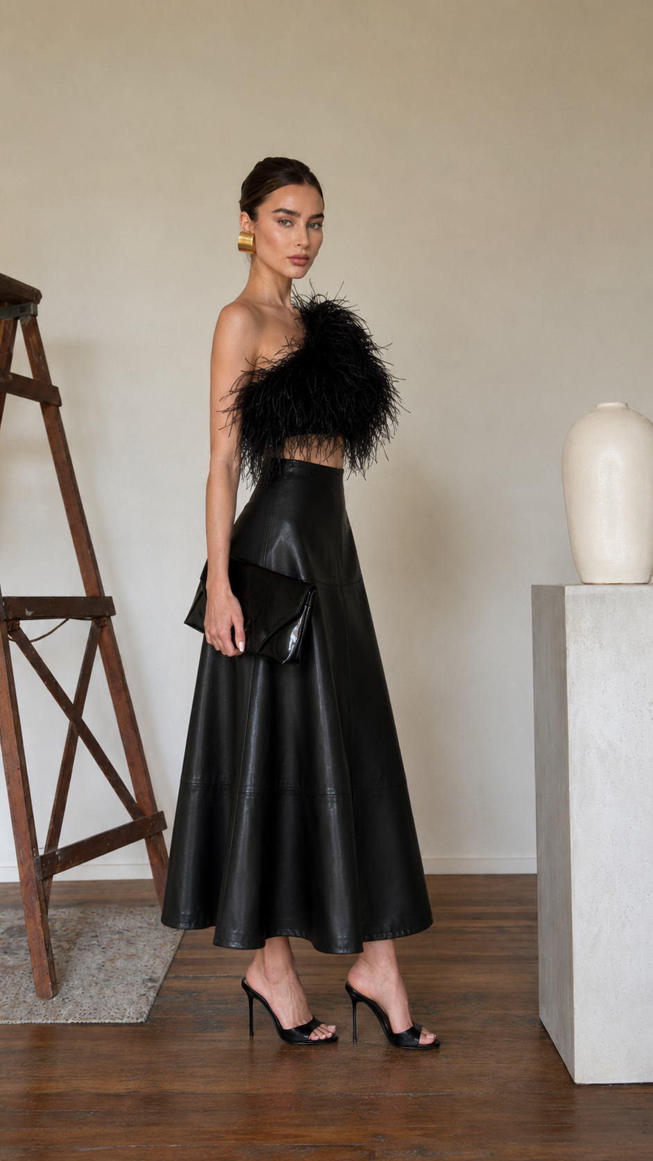 Side view of the black high-waisted faux leather A-line midi skirt styled with heels and a black clutch